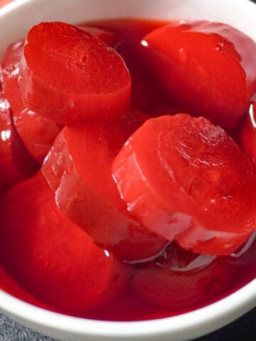 strawberry kool aid pickles and blue raspberry pickles in a white bowl sitting on a cutting board