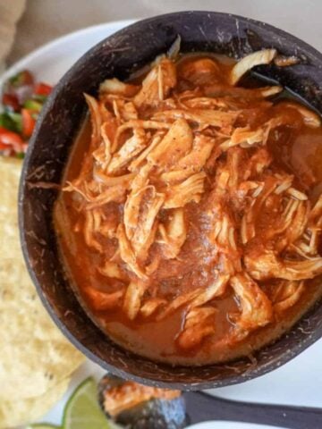 a bowl of chicken tinga with tortillas in the background