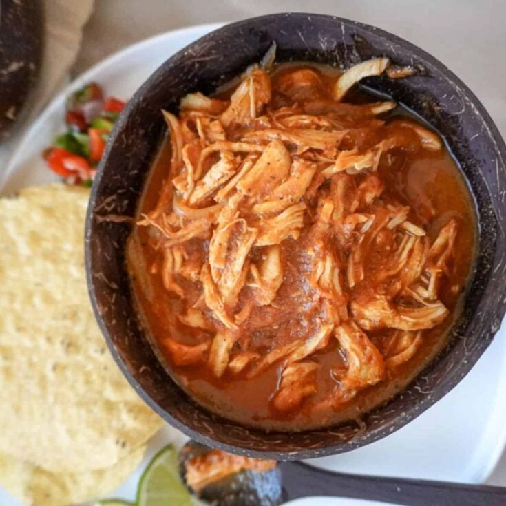 a bowl of chicken tinga with tortillas in the background