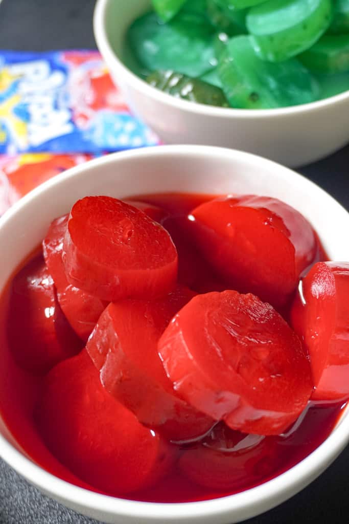 strawberry kool aid pickles and blue raspberry pickles in a white bowl sitting on a cutting board