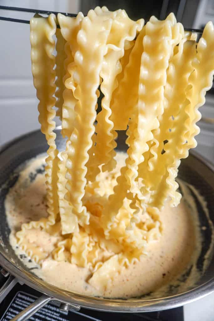 adding pasta to cheese sauce in a skillet