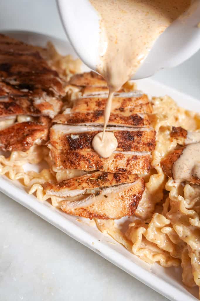 pouring extra alfredo sauce over plated chicken and pasta