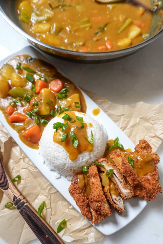 plated chicken katsu meal with a bowl of curried vegetables in the background