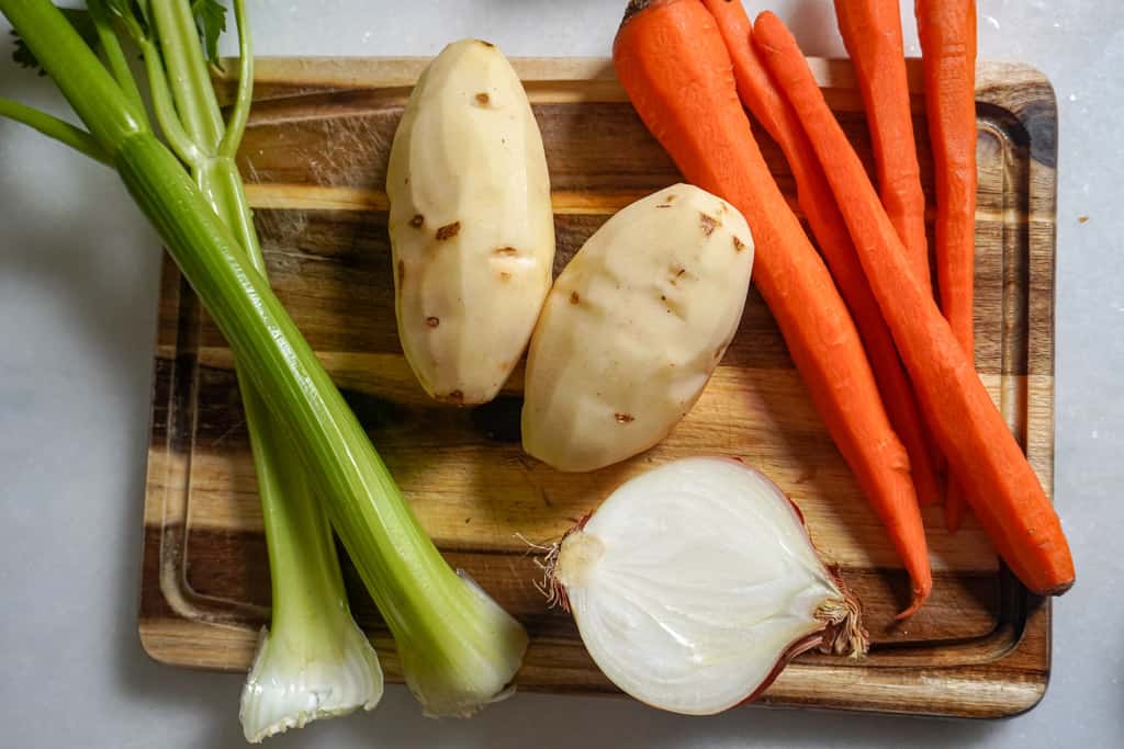 celery stalks, potatoes, carrots and half an onion on a cutting board