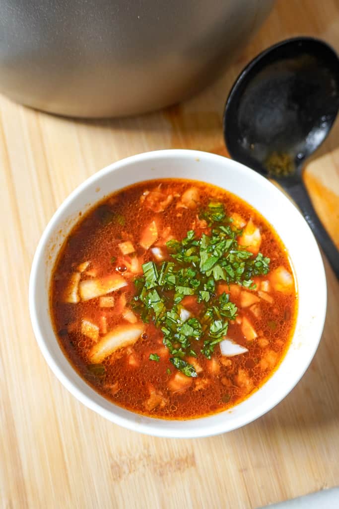 a bowl of birria consome beside a ladle