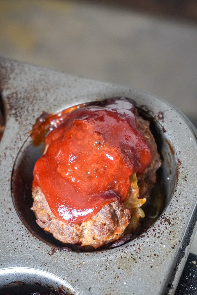 close up view of one glazed mini meatloaf in a muffin pan