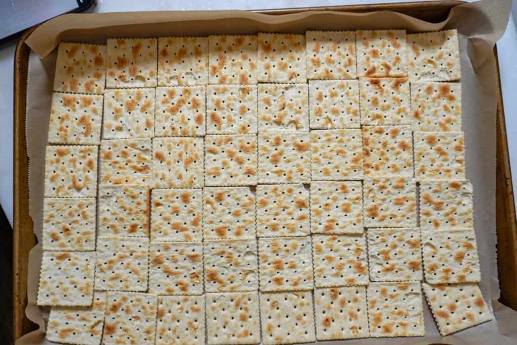 saltine crackers in a single layer on a parchment paper lined cookie sheet