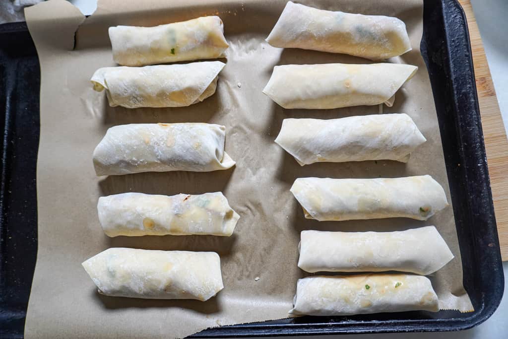 uncooked birria beef egg rolls on a parchment lined baking sheet