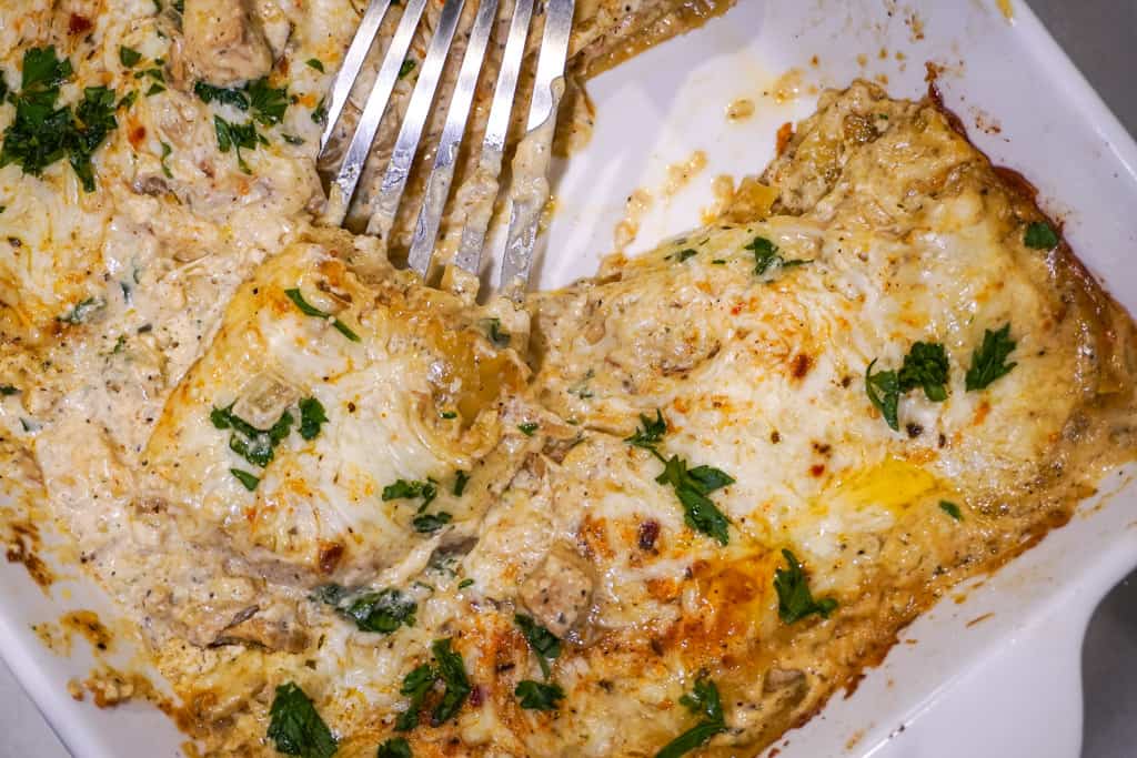 close up view of chicken alfredo lasagna in a baking dish with a spatula inserted