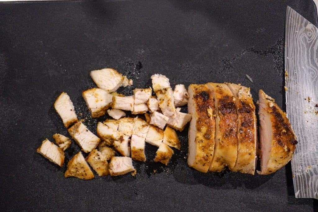 cooked, boneless chicken breast sliced and diced on a cutting board beside a large knife