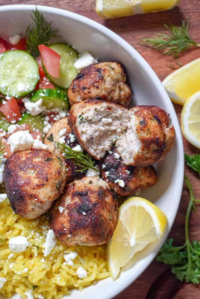 close up view of greek chicken meatballs in a yellow rice bowl