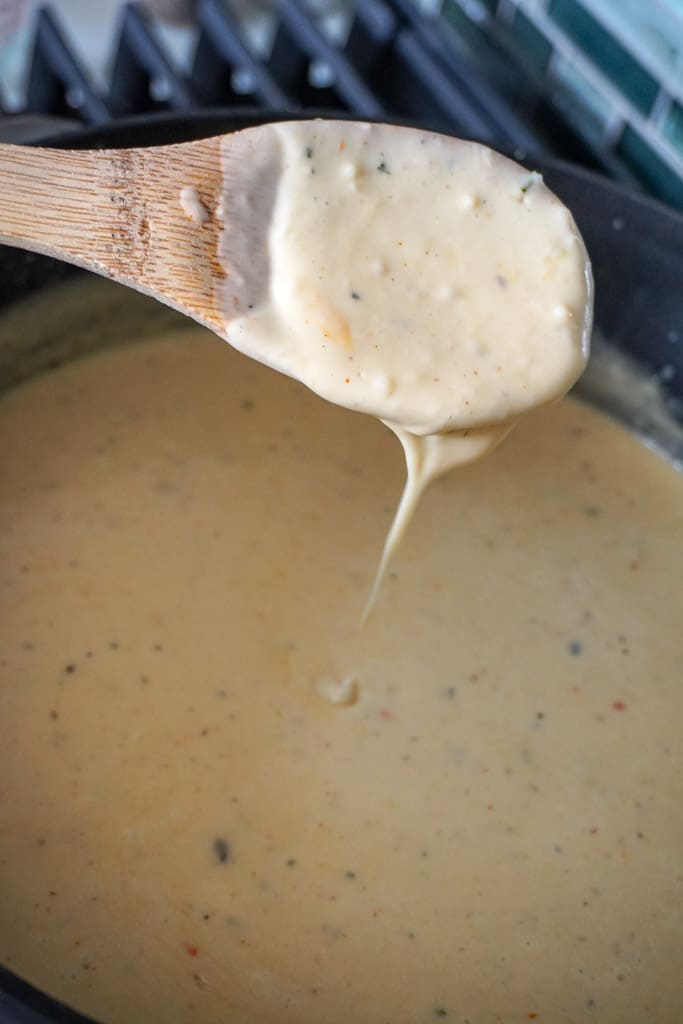 a pot of cheese sauce with a wooden spoon coated with sauce hovering over the pot
