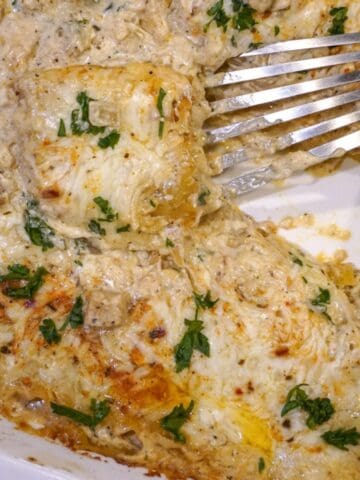 close up view of chicken alfredo lasagna in a baking dish with a spatula inserted