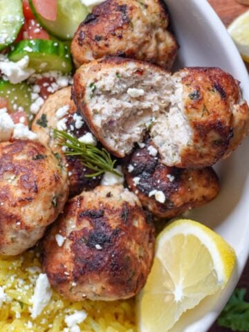 close up view of greek chicken meatballs in a yellow rice bowl
