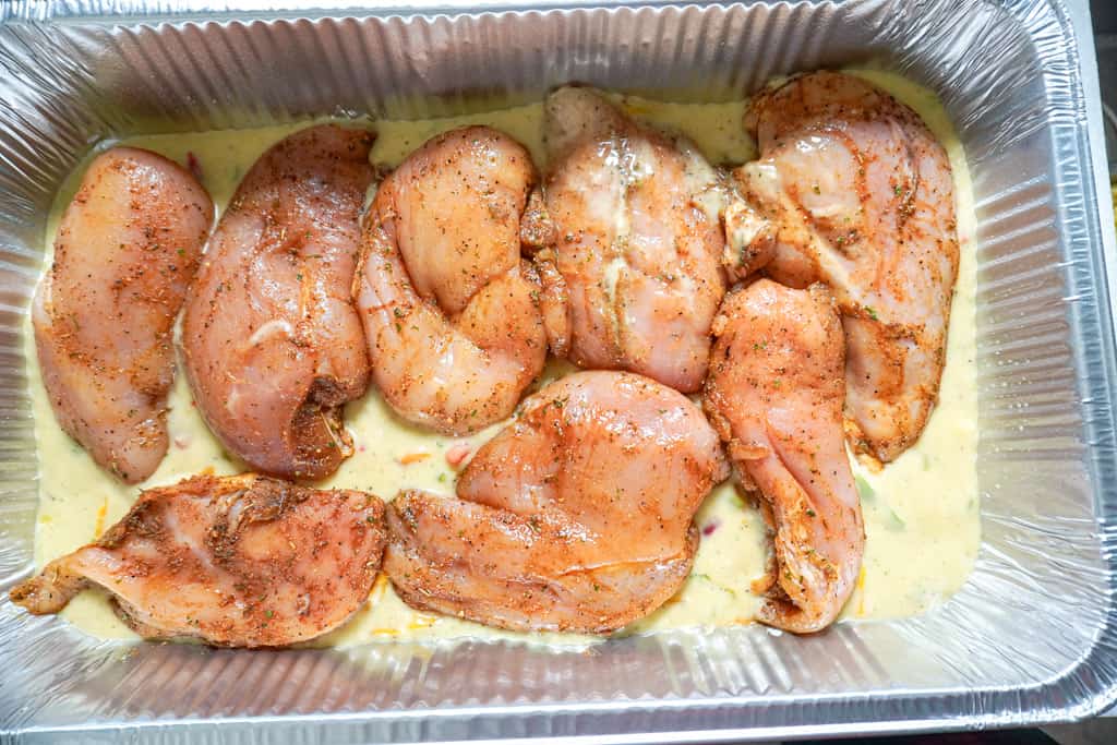 seasoned chicken over soup mixture in a foil pan
