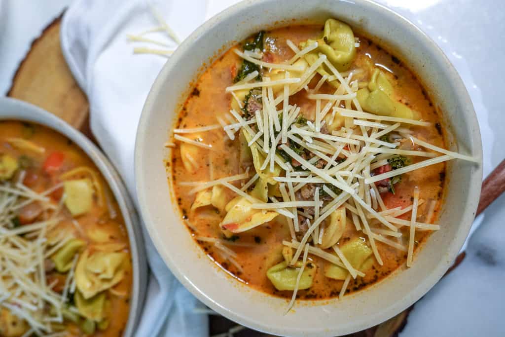 close up view of a bowl of sausage tortellini soup next to another bowl out of view