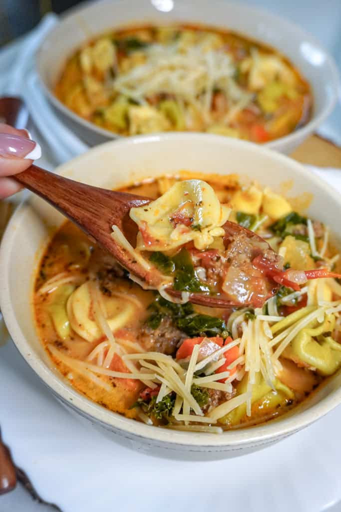 a spoon containing soup over a bowl of tortellini sausage soup