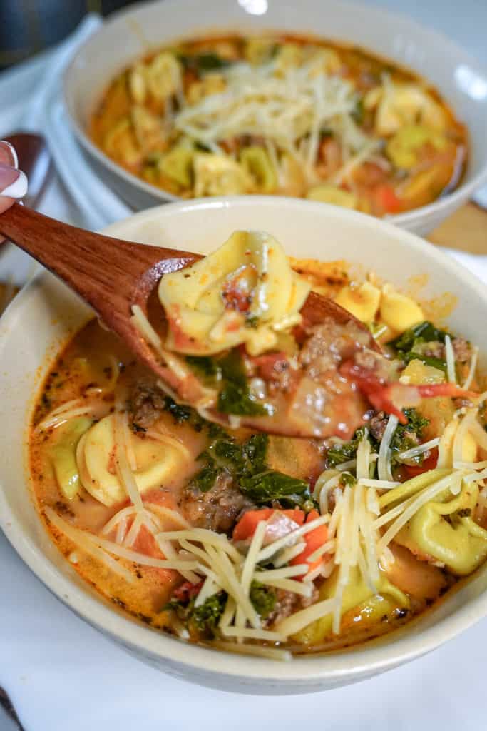 a spoon containing soup over a bowl of sausage tortellini soup