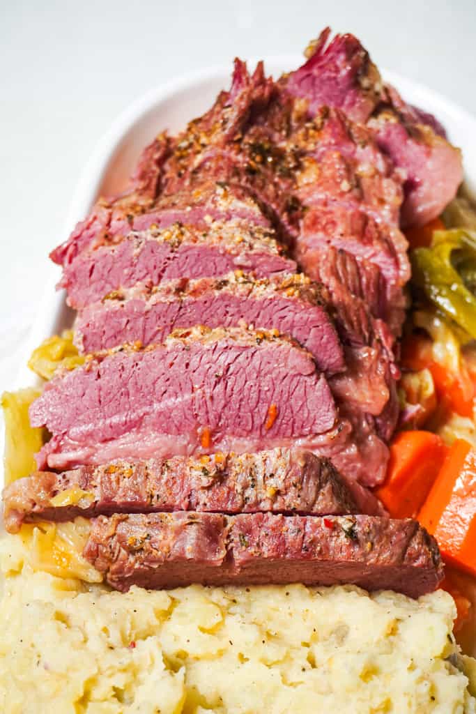 sliced corn beef plated with cabbage, carrots, and mashed potatoes