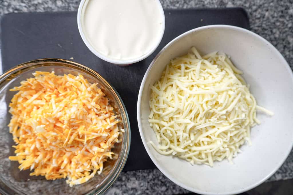 two bowls of shredded cheese beside a container of ricotta cheese