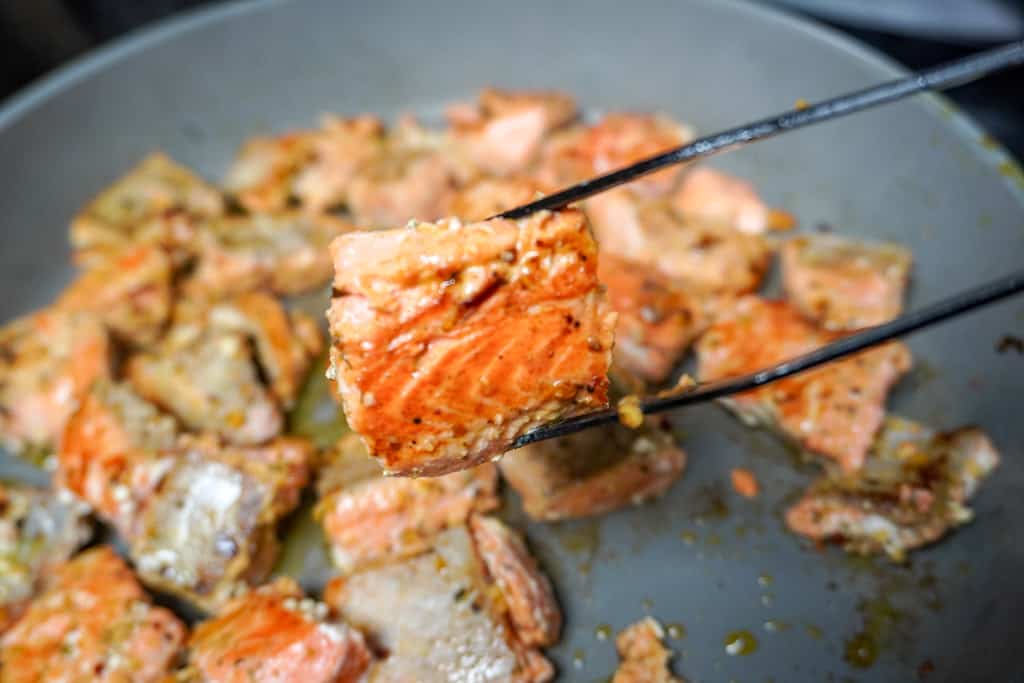 a tong holding a piece of salmon over a pan of more