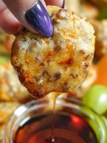 a hand dipping a pancake sausage bite into a small saucer of syrup