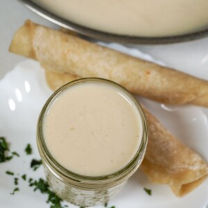 overhead view of a jar of sour cream enchilada sauce beside rolled up tortillas and a bowl containing more sauce