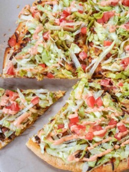 sliced taco pizza on parchment paper with one slice further away from the rest