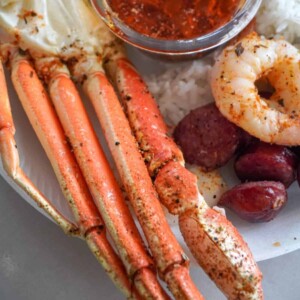 close up view of baked snow crab legs beside sausage, rice, shrimp, and seafood bake sauce