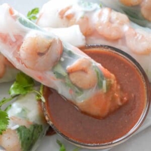 shrimp spring roll dipped in peanut sauce with more rolls scattered in the background