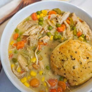 A warm bowl of chicken pot pie soup filled with shredded chicken, colorful vegetables, and topped with a golden garlic butter biscuit.