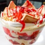 A close-up of a Strawberry Banana Pudding trifle, featuring creamy layers of pudding, fresh strawberries, bananas, Chessman cookies, and a drizzle of strawberry glaze on top.
