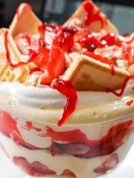 A close-up of a Strawberry Banana Pudding trifle, featuring creamy layers of pudding, fresh strawberries, bananas, Chessman cookies, and a drizzle of strawberry glaze on top.