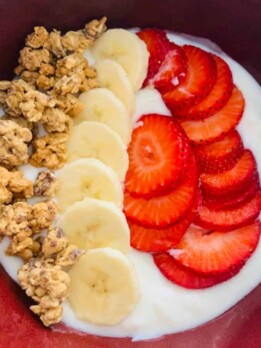 a bowl of yogurt parfait topped with fresh sliced fruit and granola