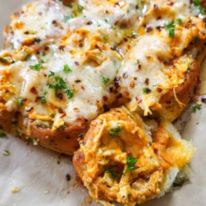 Close-up of Buffalo chicken sliders topped with melted cheese, parsley, and red pepper flakes.