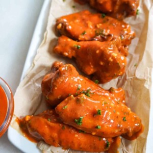 A close-up of saucy baked buffalo chicken wings garnished with parsley, served on parchment paper.