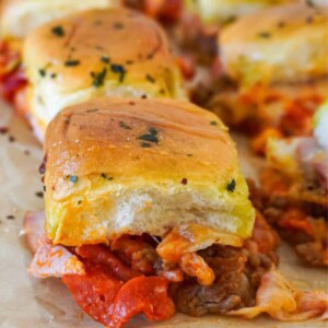 A tray of meat lovers pizza sliders with crispy tops, melted cheese, and layers of pepperoni, sausage, and Canadian bacon.