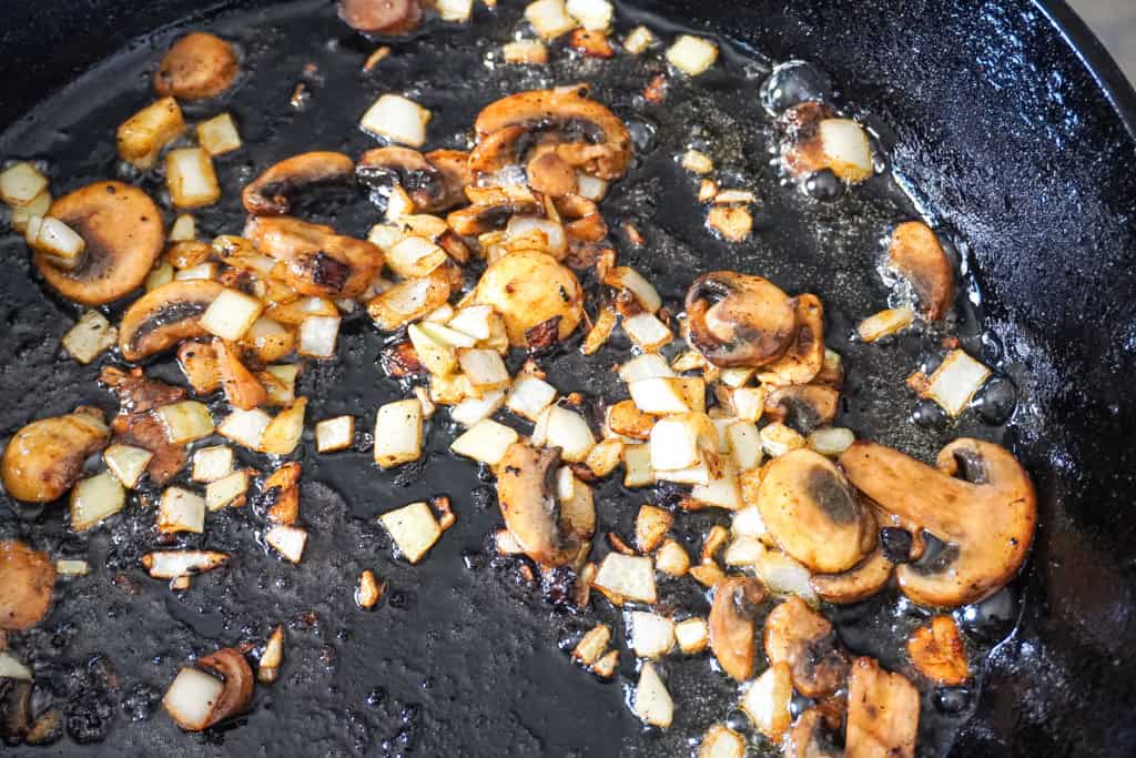 Sautéed mushrooms and diced onions browning in a cast iron skillet.