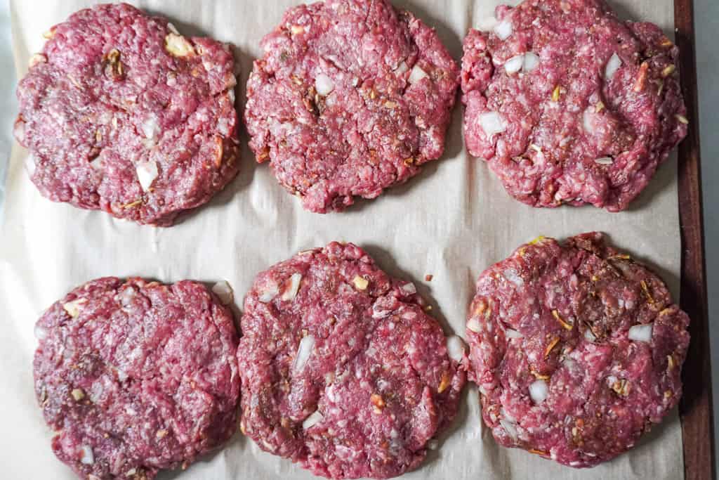 Six raw hamburger steak patties arranged on parchment paper, ready for cooking.