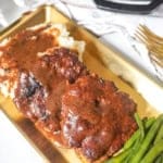 A golden platter with juicy hamburger steaks draped in thick brown gravy, alongside mashed potatoes and green beans.