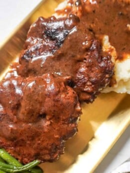 A serving of hamburger steaks with brown gravy, mashed potatoes, and green beans.