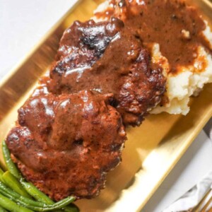 A serving of hamburger steaks with brown gravy, mashed potatoes, and green beans.