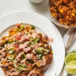 A plate of taco rice topped with melted cheese, fresh lettuce, diced tomatoes, and a creamy sauce, served alongside a bowl filled with the same flavorful mixture.