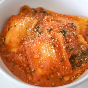 Close-up of cheese ravioli in creamy tomato sauce, sprinkled with grated Parmesan.