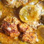 Close-up of slow cooker chicken thighs simmering in a seasoned lemon butter sauce.