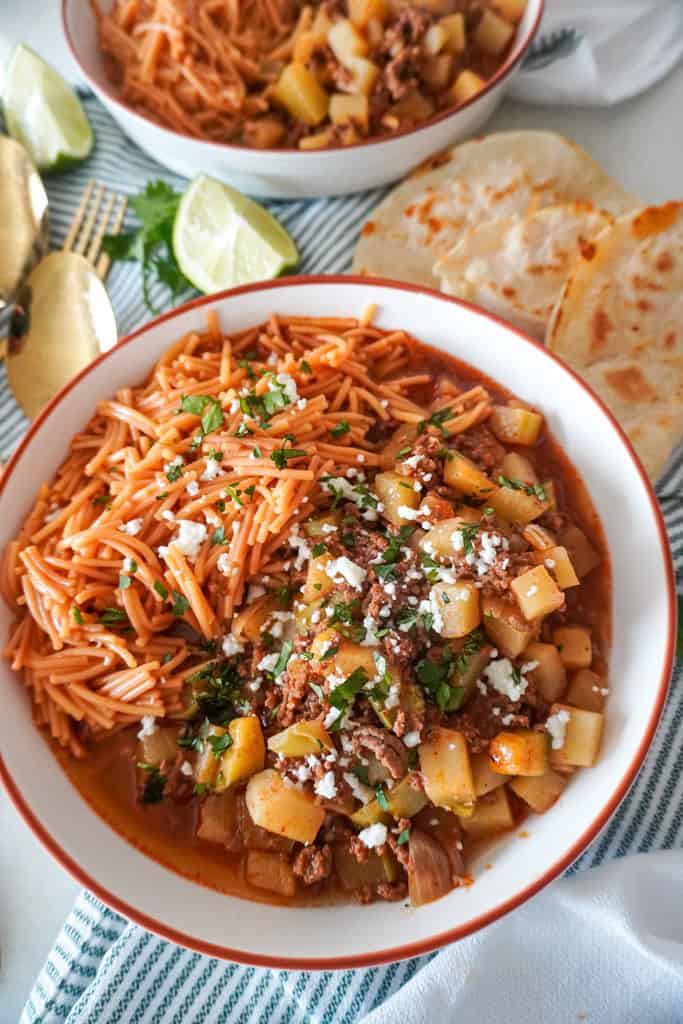 picadillo or ground beef with potatoes in a white bowl with quesadillas next to it on a table