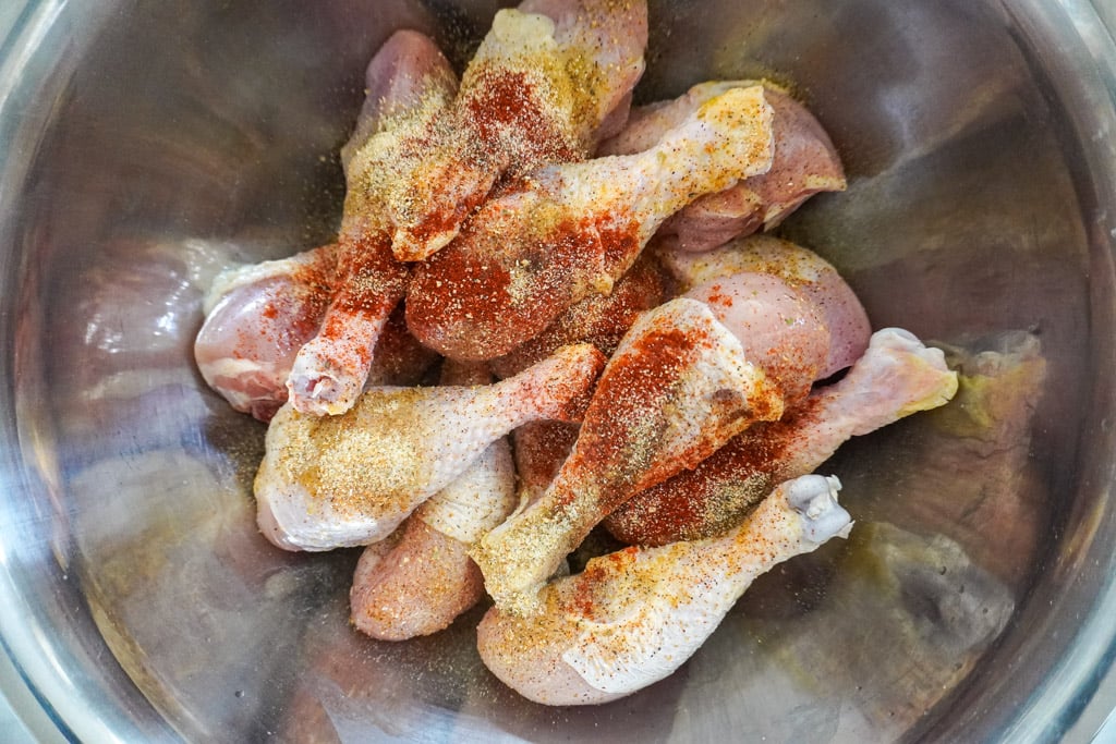 chicken drumsticks in a bowl with seasoning on them