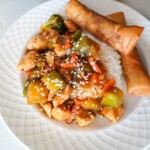 teriyaki chicken stir fry plated with rice and egg rolls