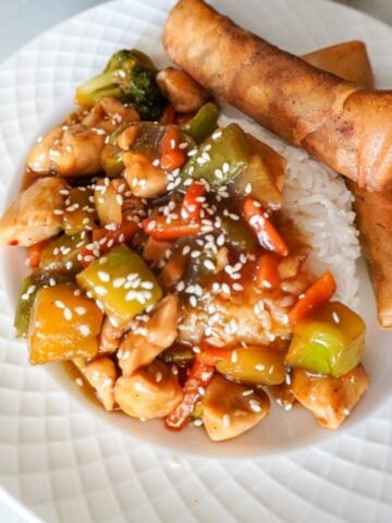 teriyaki chicken stir fry plated with rice and egg rolls