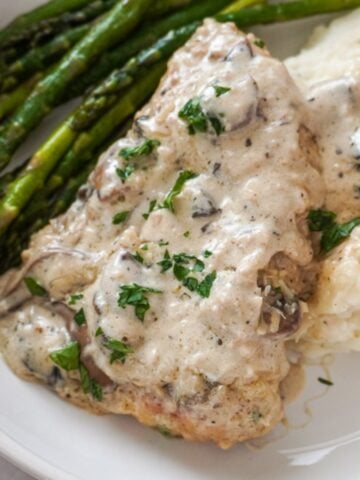 garlic parmesan chicken on a plate with mashed potatoes and asparagus